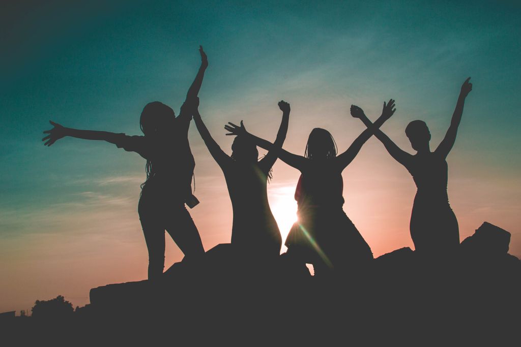 Four women enjoying a fun silhouette moment during a vibrant Kenyan sunset.